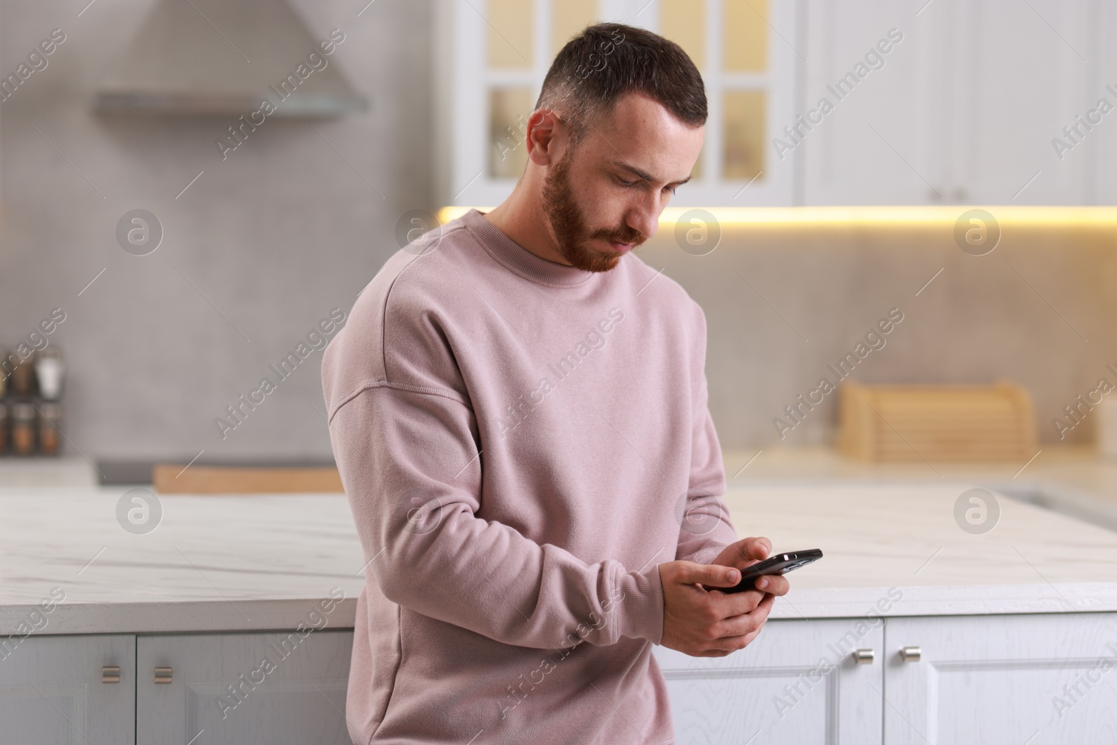 Photo of Handsome man looking at smartphone in kitchen