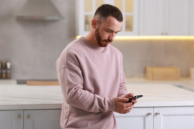 Photo of Handsome man looking at smartphone in kitchen