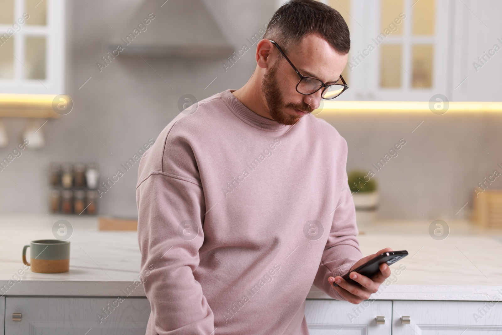 Photo of Handsome man looking at smartphone in kitchen