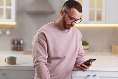 Handsome man looking at smartphone in kitchen