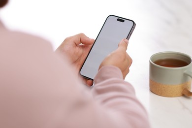 Man using smartphone at white table with cup of tea, closeup