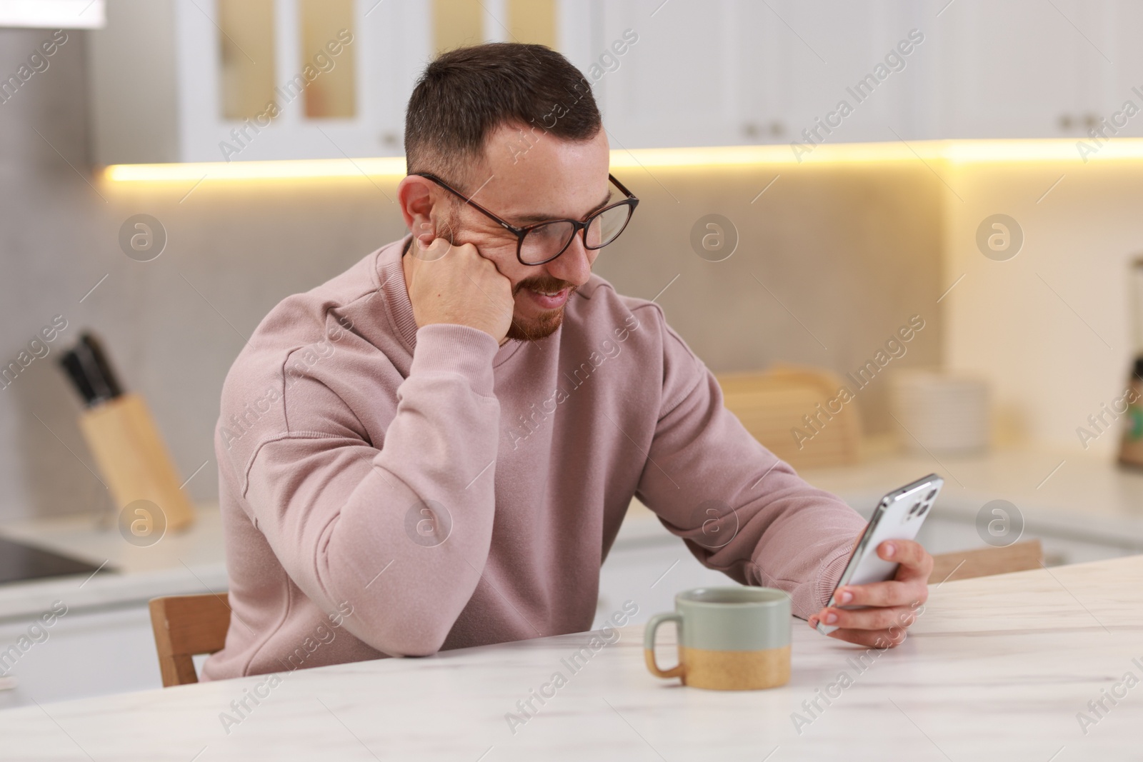 Photo of Happy man using smartphone at white table in kitchen