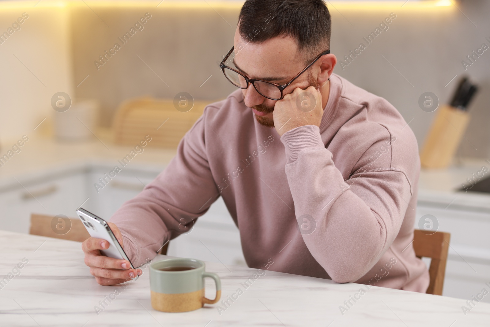 Photo of Handsome man using smartphone at white table in kitchen