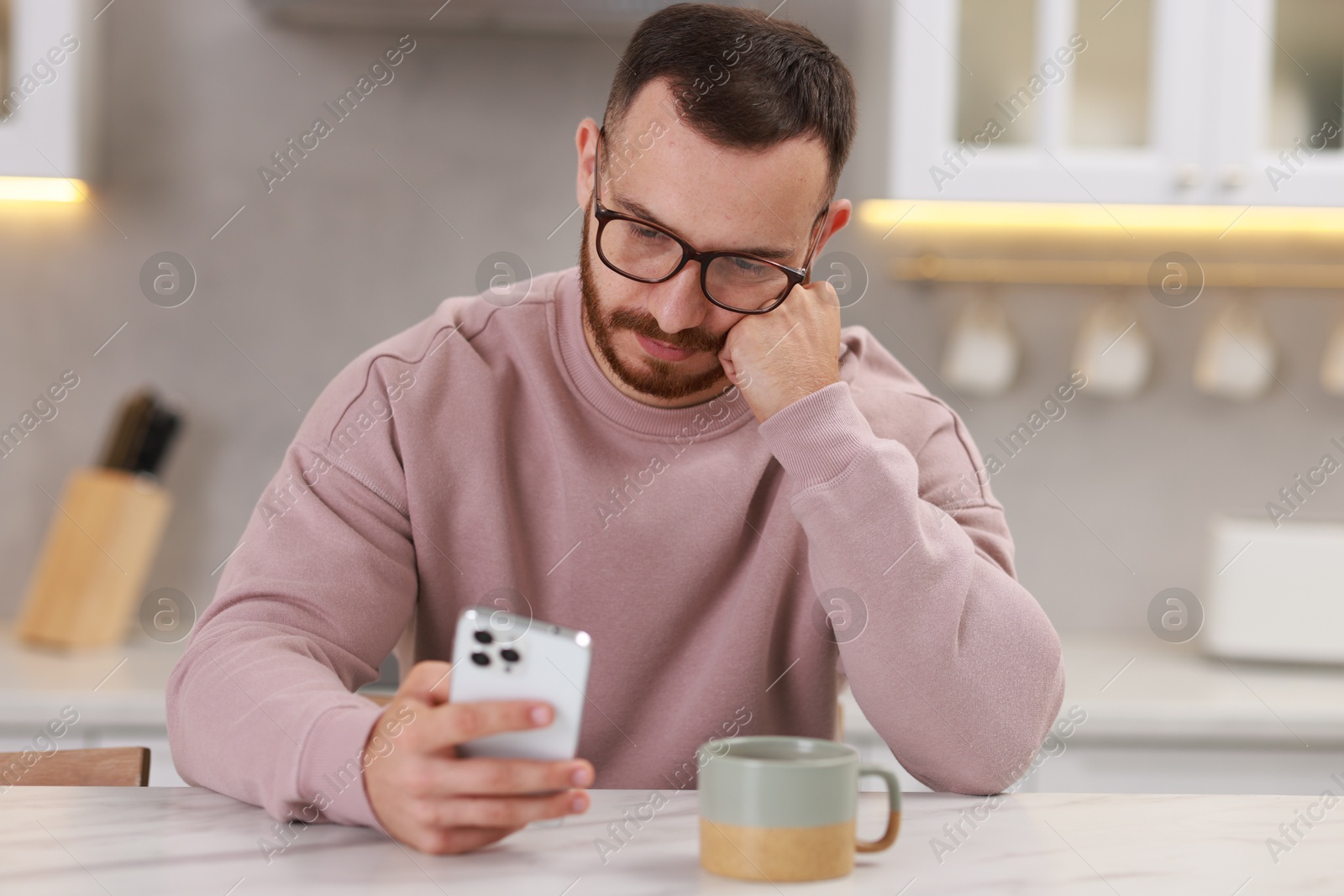 Photo of Handsome man using smartphone at white table in kitchen