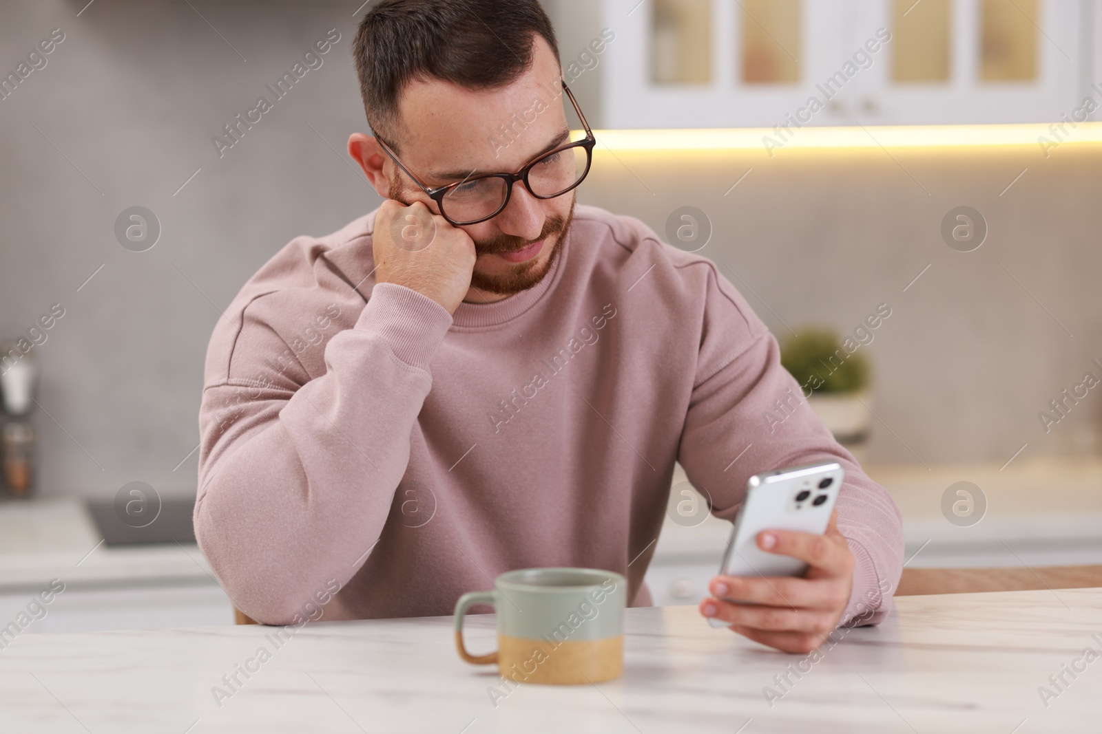 Photo of Handsome man using smartphone at white table in kitchen