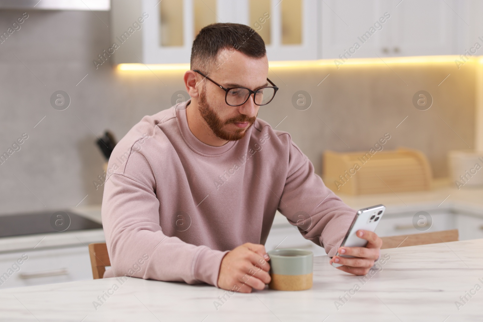 Photo of Handsome man using smartphone at white table in kitchen