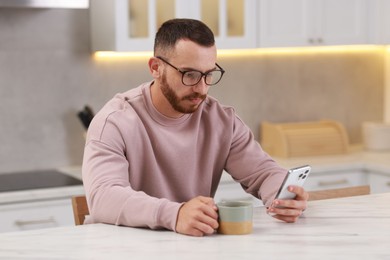 Photo of Handsome man using smartphone at white table in kitchen