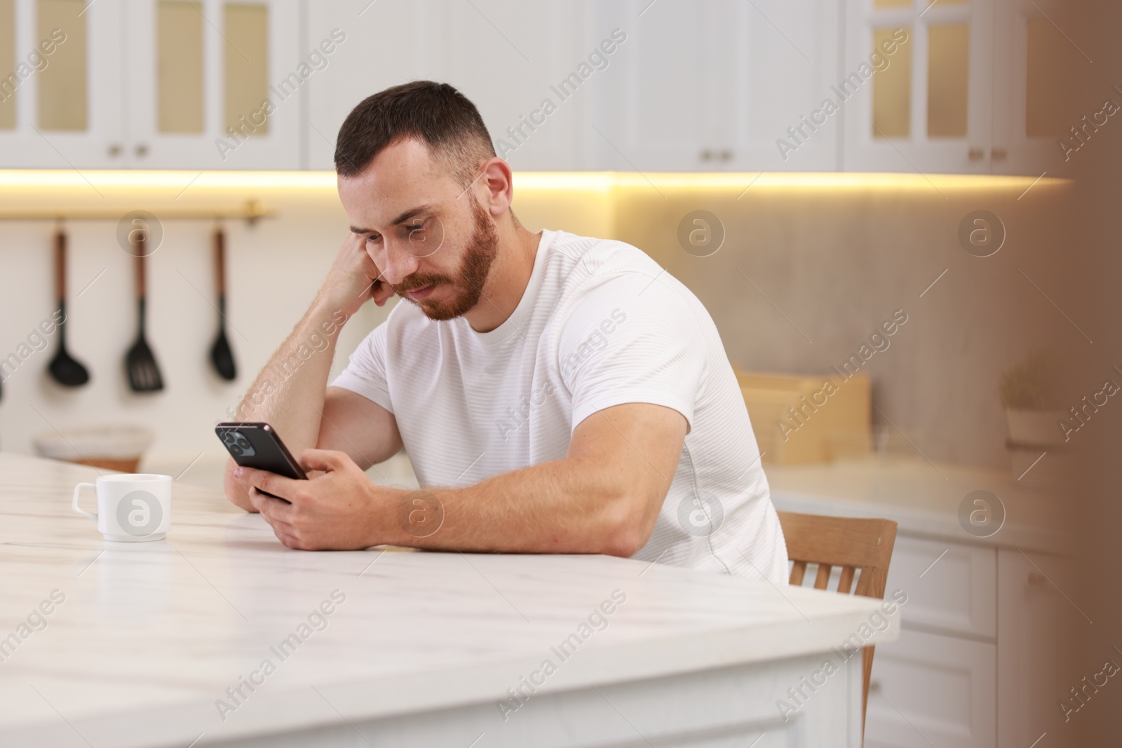 Photo of Handsome man looking at smartphone in kitchen