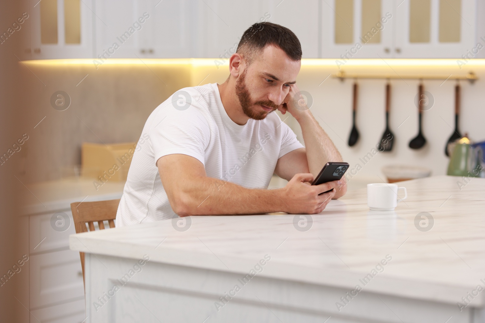 Photo of Handsome man looking at smartphone in kitchen