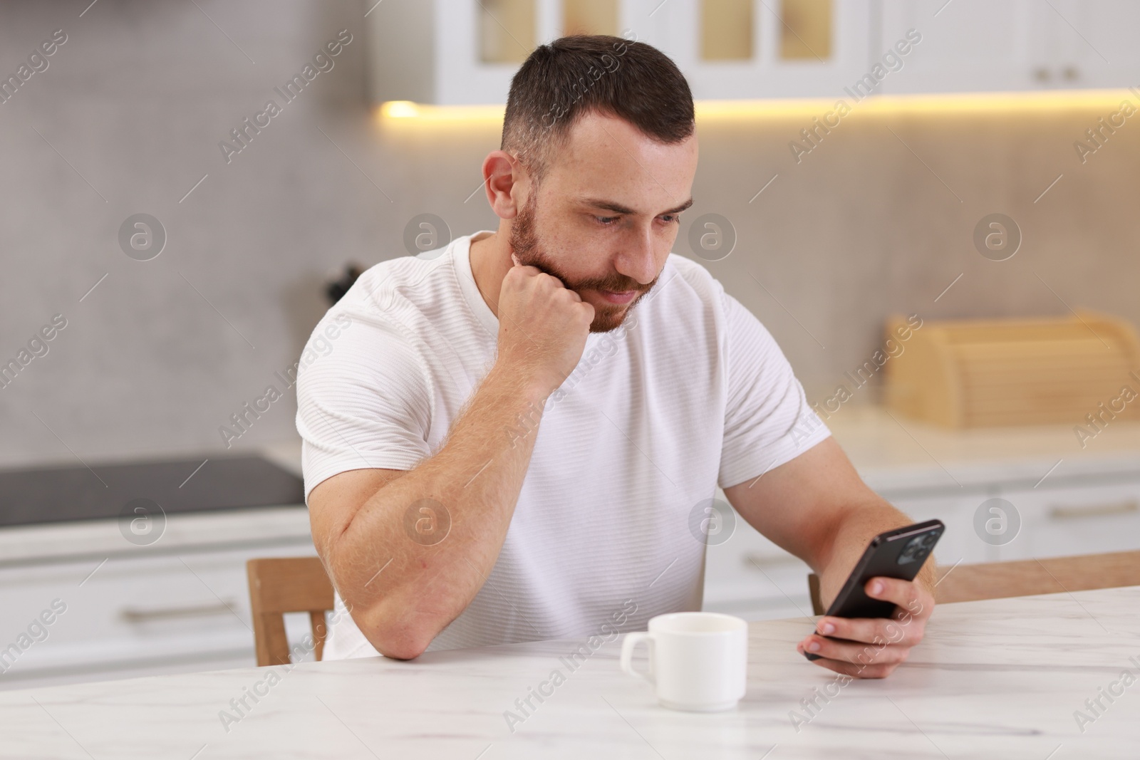 Photo of Handsome man using smartphone at white table in kitchen