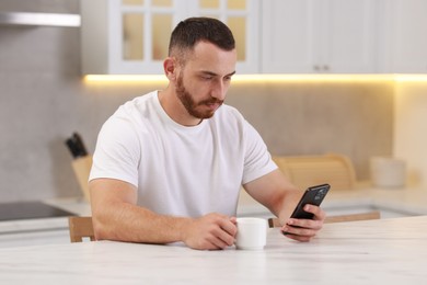 Photo of Handsome man using smartphone at white table in kitchen