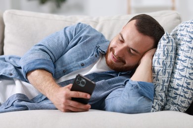 Photo of Handsome man looking at smartphone on sofa