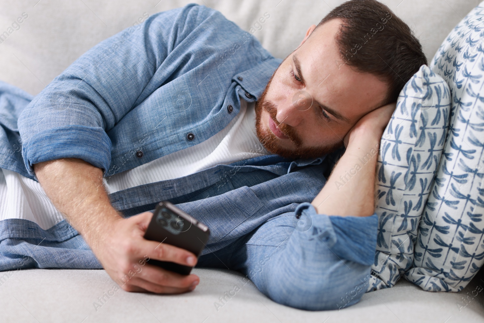 Photo of Handsome man looking at smartphone on sofa