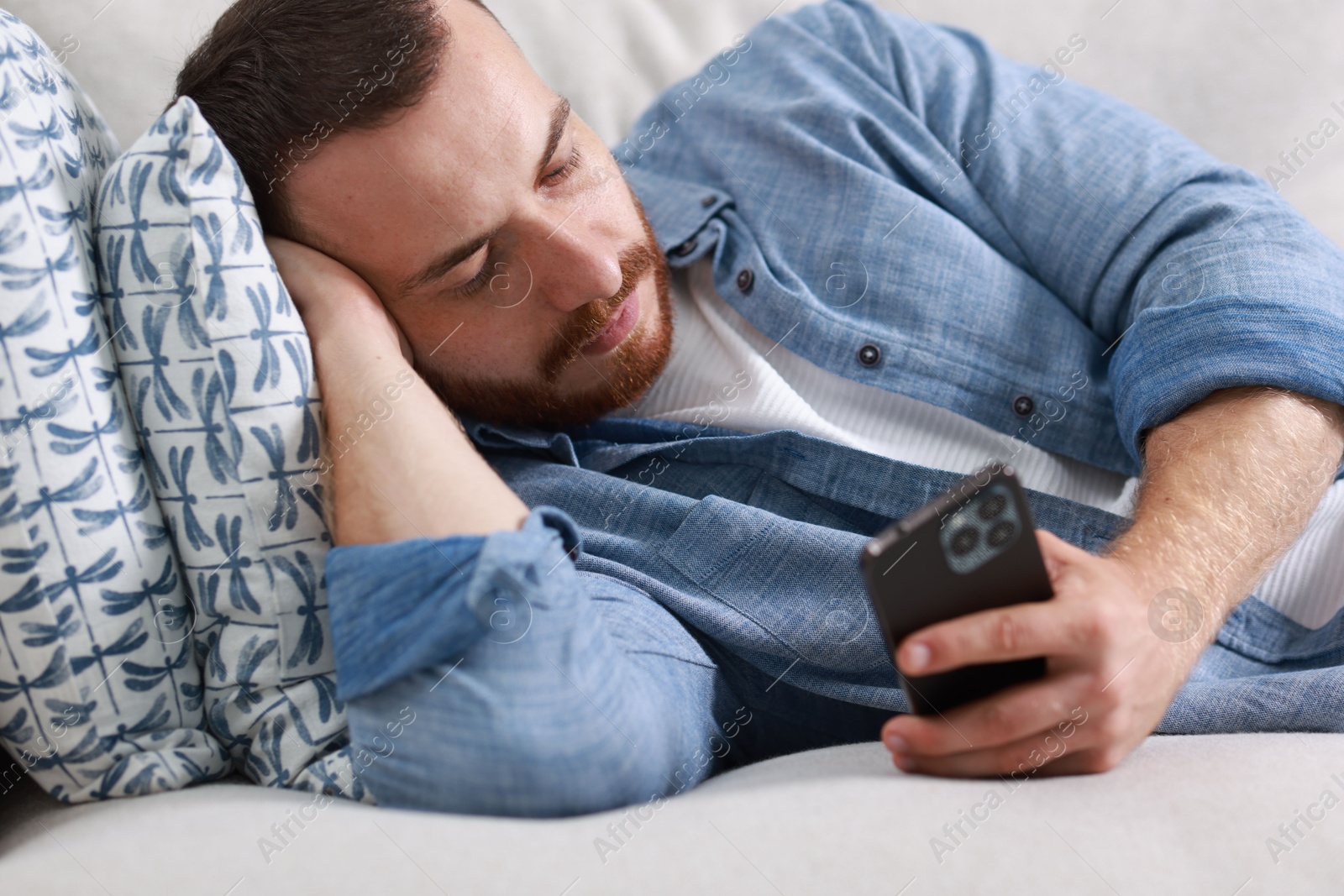 Photo of Handsome man looking at smartphone on sofa