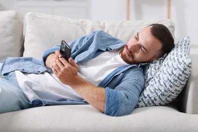 Handsome man looking at smartphone on sofa