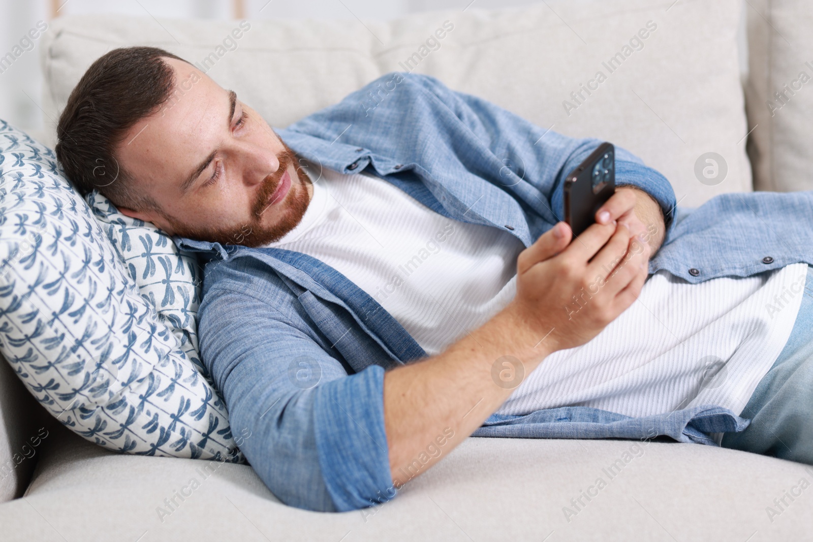 Photo of Handsome man looking at smartphone on sofa