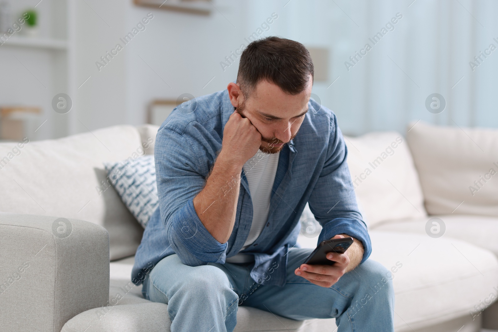 Photo of Handsome man looking at smartphone on sofa indoors