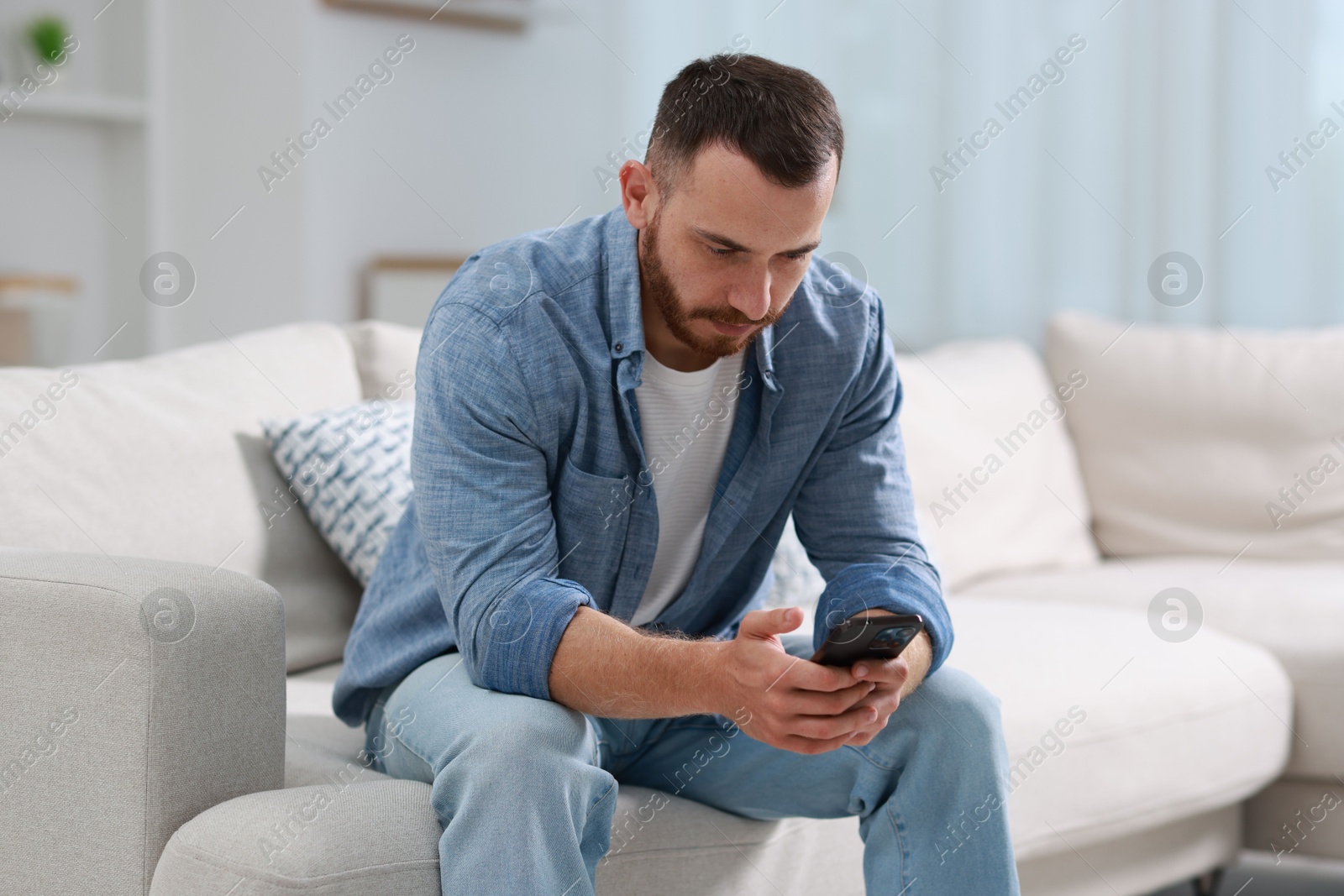 Photo of Handsome man using smartphone on sofa indoors