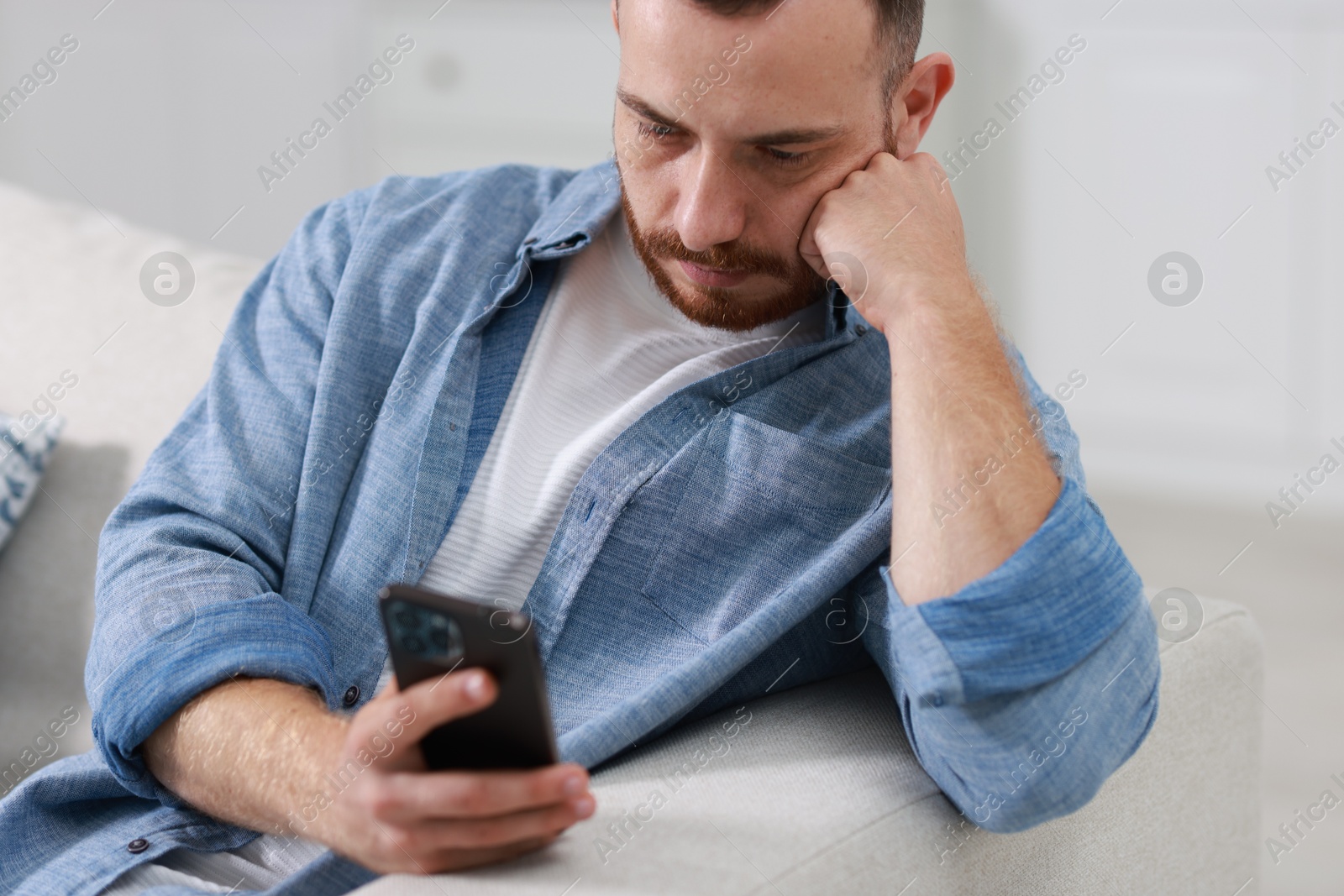 Photo of Handsome man using smartphone on sofa indoors