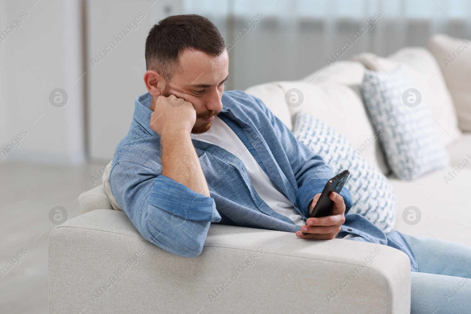 Photo of Handsome man using smartphone on sofa indoors