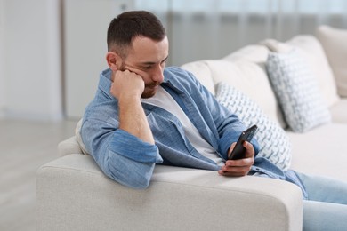 Handsome man using smartphone on sofa indoors