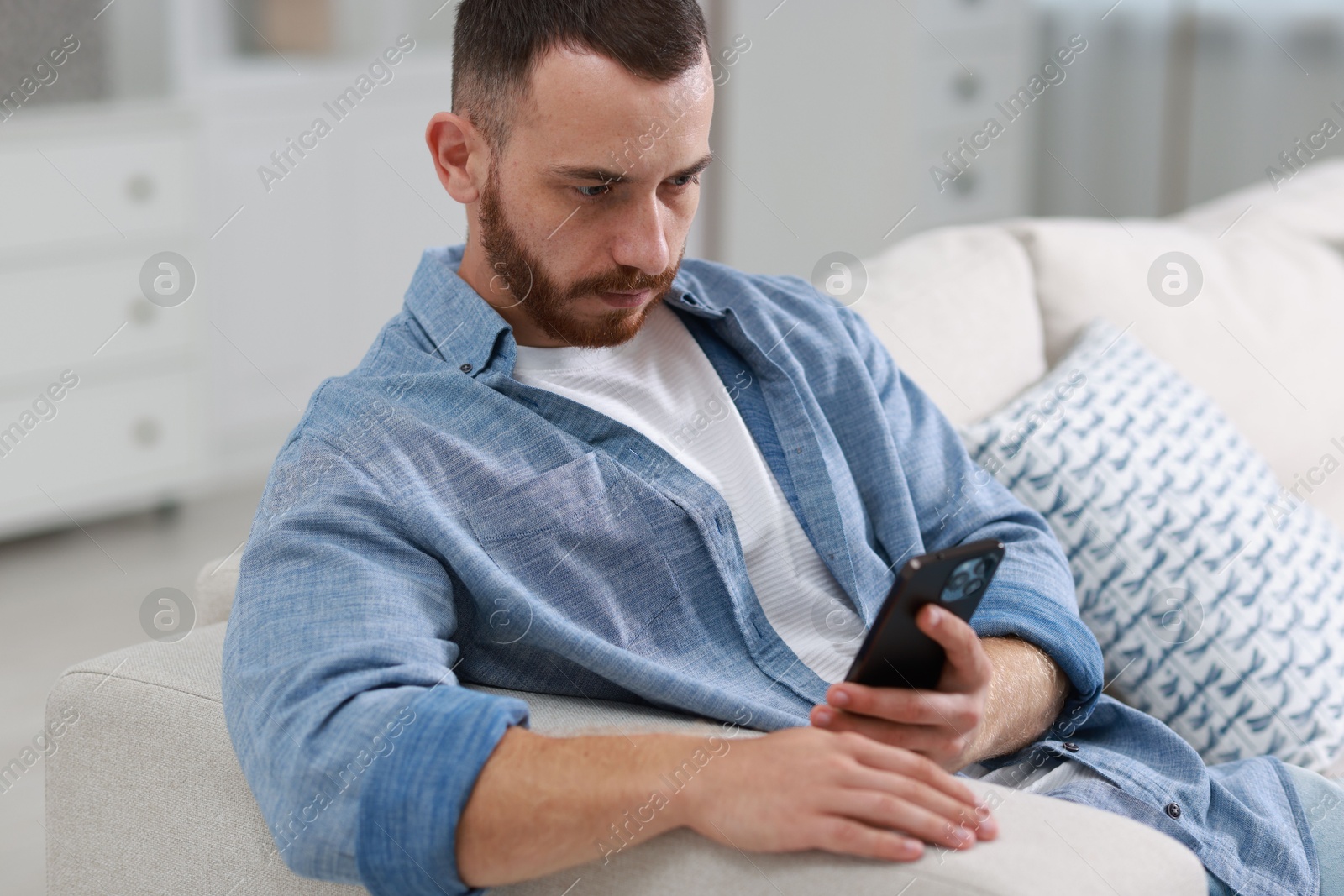 Photo of Handsome man using smartphone on sofa indoors