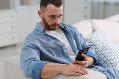 Handsome man using smartphone on sofa indoors