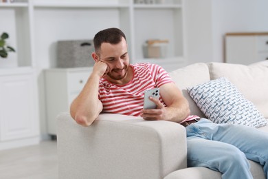 Photo of Handsome man using smartphone on sofa indoors