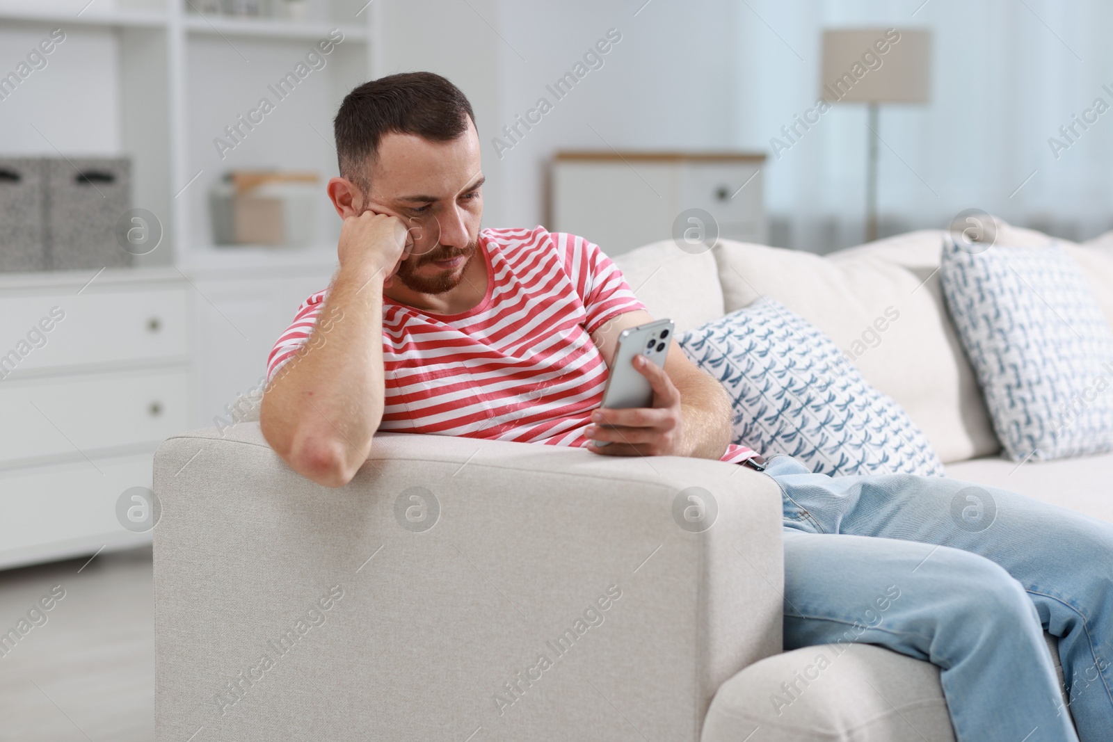 Photo of Handsome man using smartphone on sofa indoors