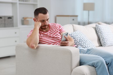 Handsome man using smartphone on sofa indoors