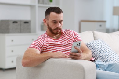 Handsome man using smartphone on sofa indoors