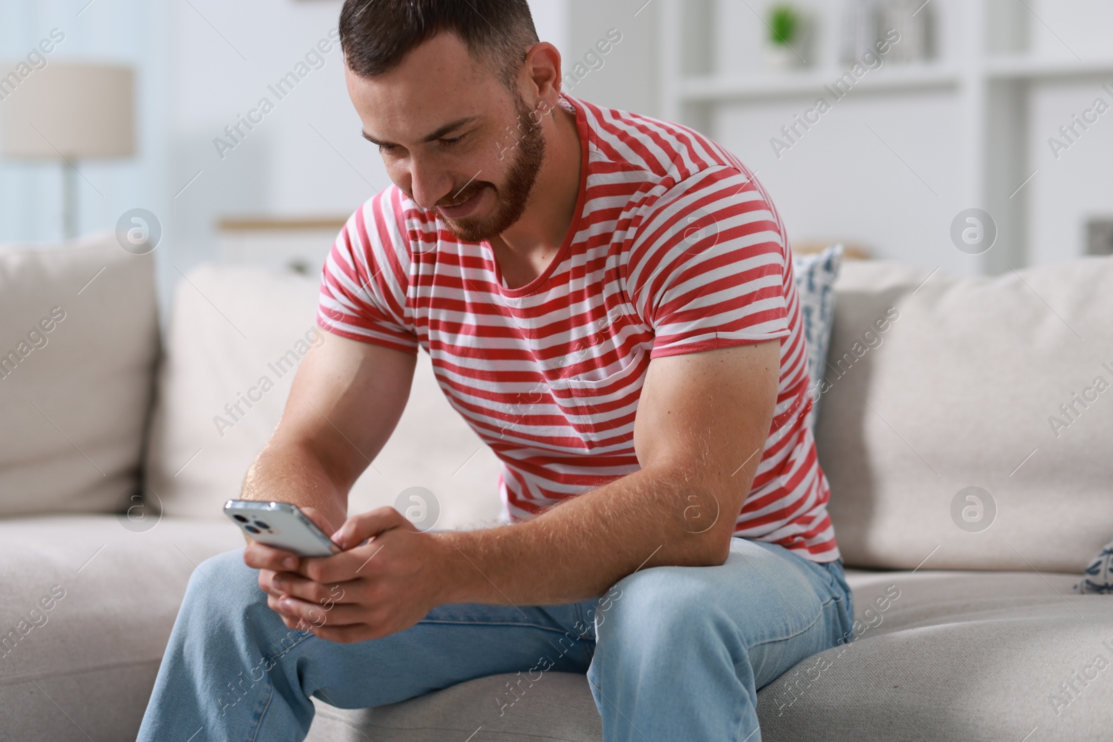 Photo of Handsome man using smartphone on sofa indoors