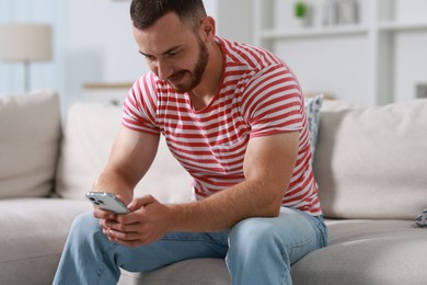 Handsome man using smartphone on sofa indoors