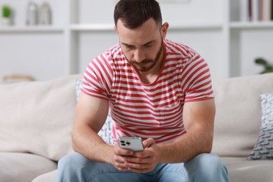 Photo of Handsome man using smartphone on sofa indoors