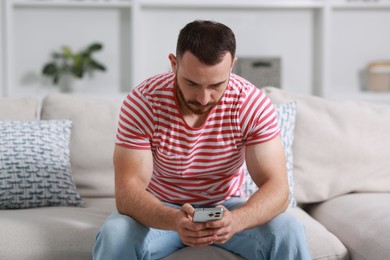 Photo of Handsome man using smartphone on sofa indoors