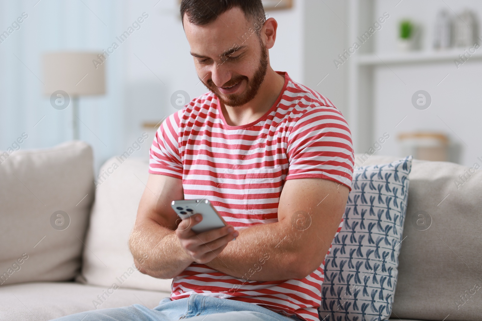 Photo of Happy man using smartphone on sofa indoors