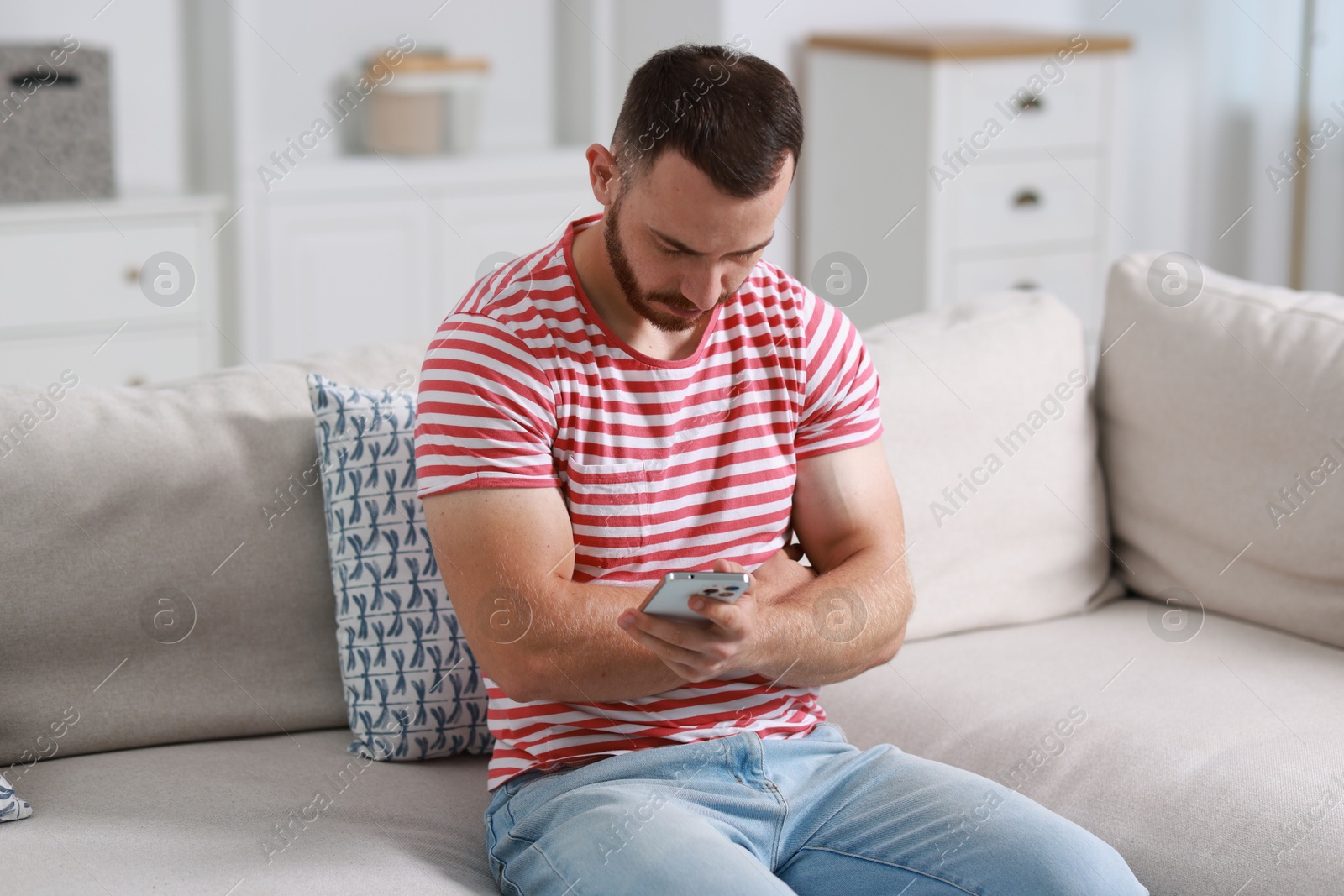 Photo of Handsome man using smartphone on sofa indoors