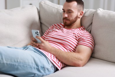 Photo of Handsome man using smartphone on sofa indoors