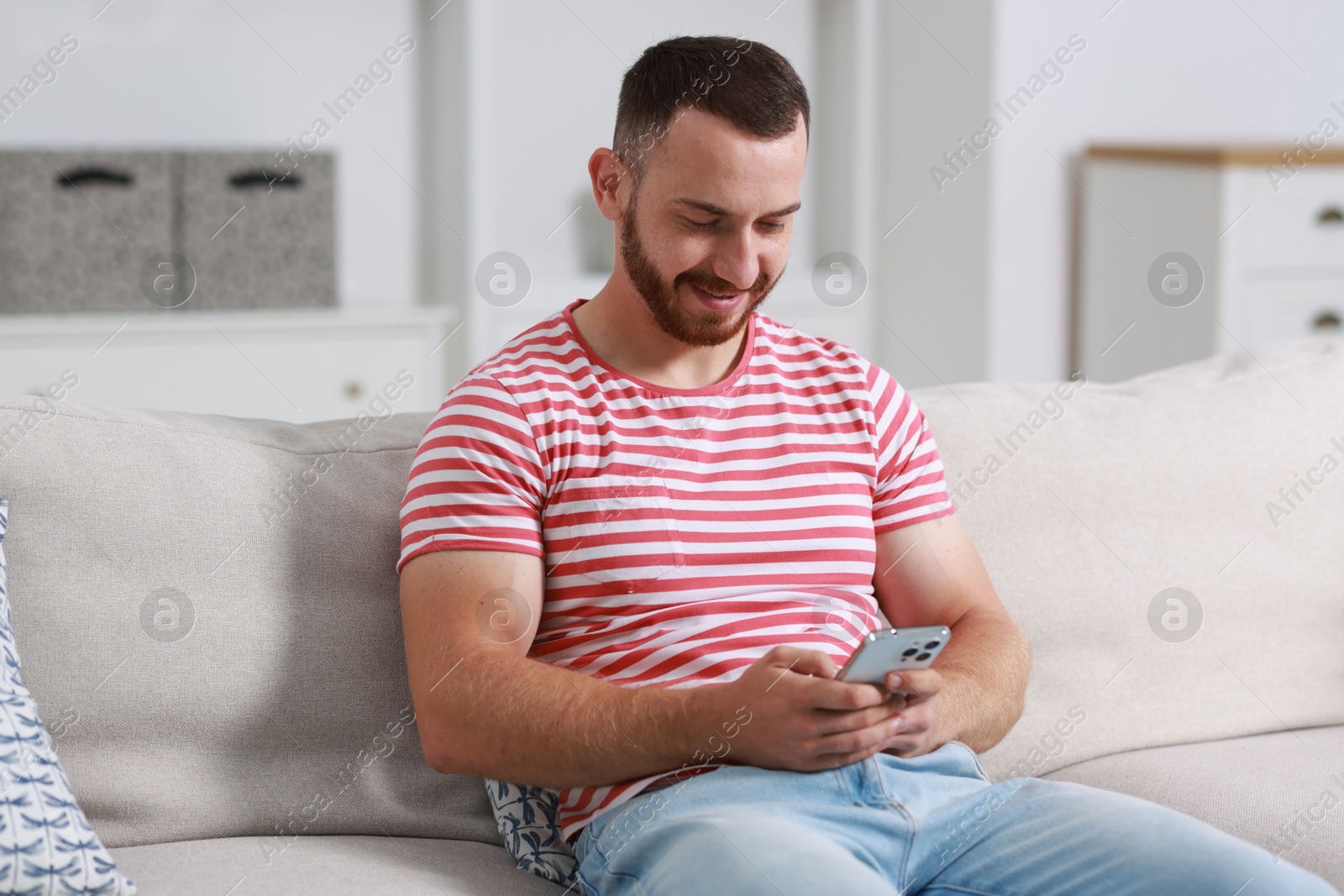 Photo of Handsome man using smartphone on sofa indoors