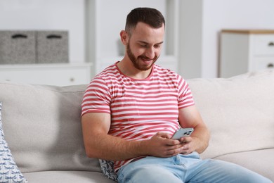 Handsome man using smartphone on sofa indoors