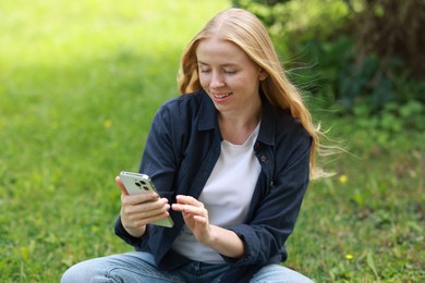 Photo of Smiling woman using smartphone on green grass outdoors