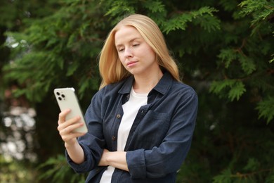 Beautiful woman using smartphone near tree outdoors