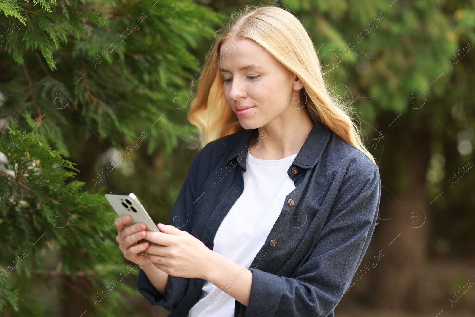 Photo of Beautiful woman using smartphone near tree outdoors