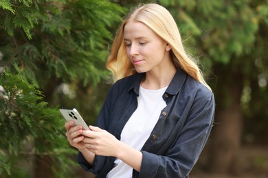 Beautiful woman using smartphone near tree outdoors