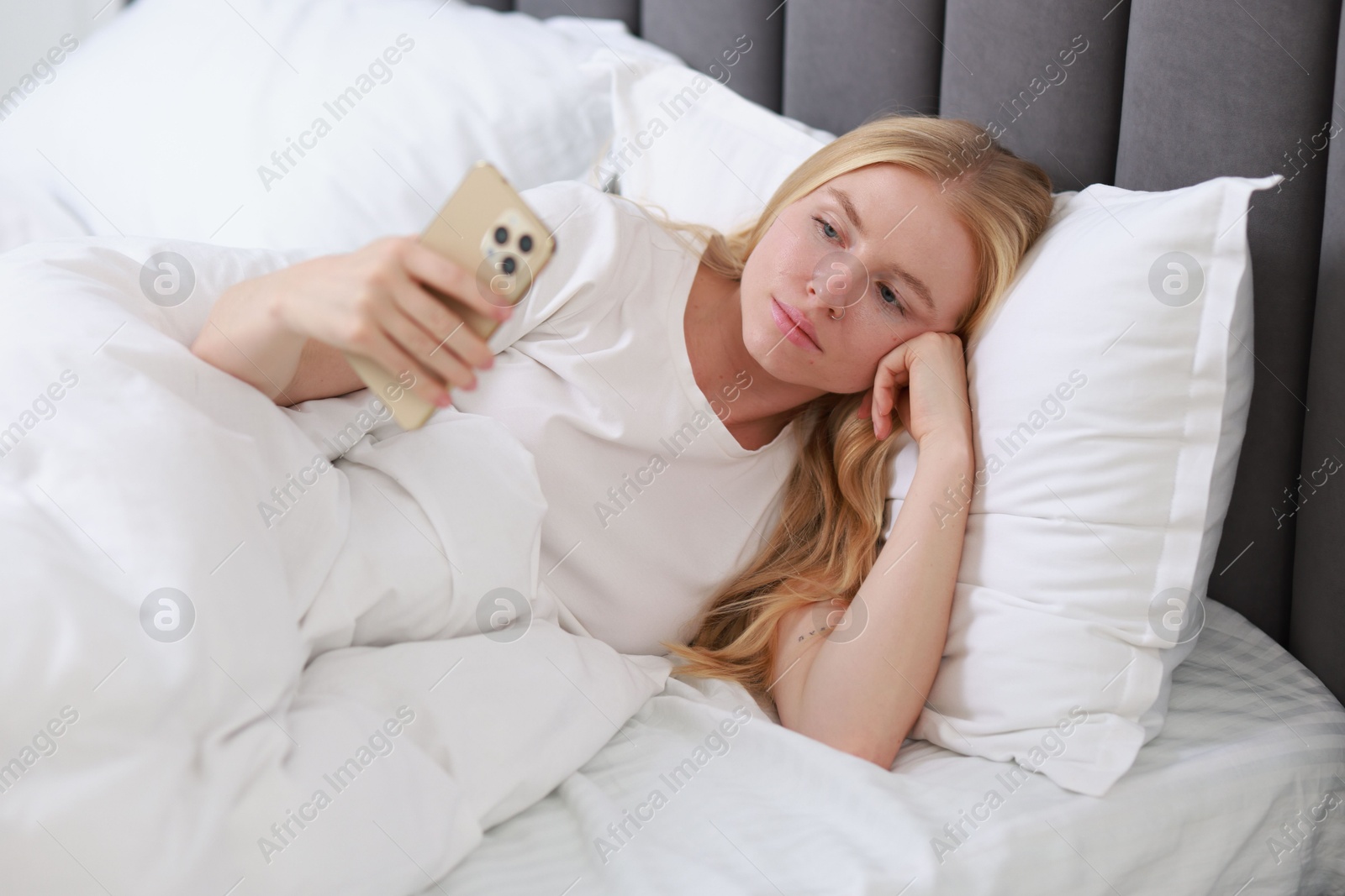 Photo of Beautiful woman looking at smartphone in bed