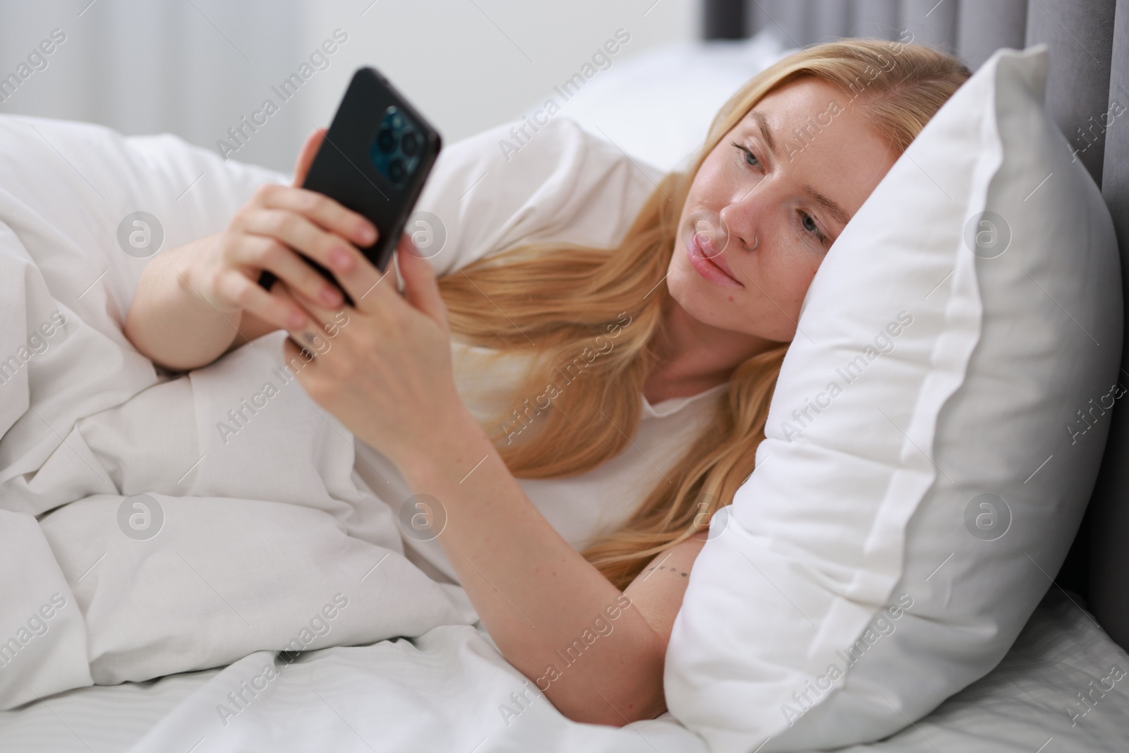 Photo of Beautiful woman looking at smartphone in bed