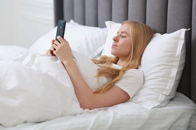 Beautiful woman looking at smartphone in bed