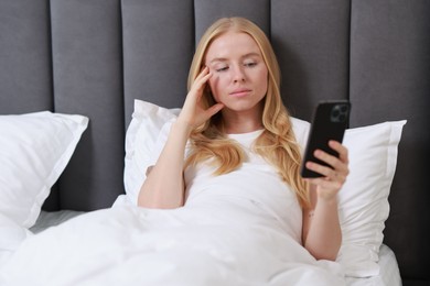 Beautiful woman looking at smartphone in bed