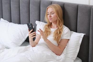 Photo of Beautiful woman looking at smartphone in bed