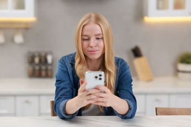 Photo of Beautiful woman using smartphone at white table in kitchen